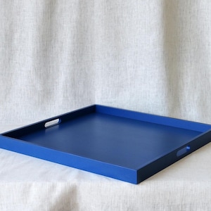 Puede incluir: Una bandeja rectangular grande de madera con un acabado azul oscuro. La bandeja tiene dos asas recortadas a cada lado.