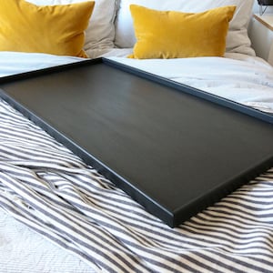 May include: A black wooden tray sits on a striped bedspread. The tray is rectangular and has a smooth surface.