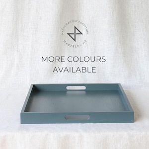 Może przedstawiać: Prostokątna taca do serwowania w kolorze turkusowym z dwoma uchwytami po obu stronach. Taca wykonana jest z drewna i ma gładkie wykończenie. Tekst "MORE COLOURS AVAILABLE" jest nadrukowany czarnym kolorem na białym tle nad tacą.