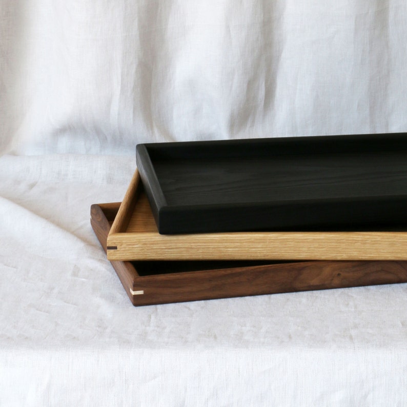 Close up of the 3 colour options of the ottoman trays, from top - black, oak and walnut.