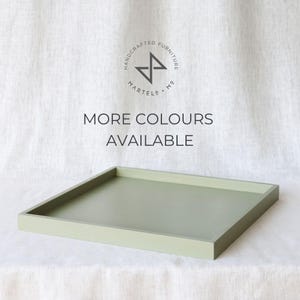 Pode incluir: Uma bandeja retangular de cor verde claro com uma borda elevada. A bandeja é feita de madeira e tem um acabamento liso. O texto "MORE COLOURS AVAILABLE" está impresso em preto sobre fundo branco.