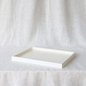 Puede incluir: Una bandeja rectangular blanca para servir con un borde elevado. La bandeja está hecha de madera y tiene un acabado liso y pulido.