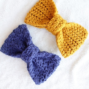May include: Two crocheted bows, one in a deep blue and one in a mustard yellow. The bows are made with a textured stitch and are tied in a simple knot.