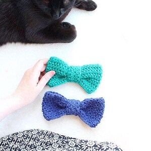 May include: Two crocheted bow ties, one teal and one navy blue, on a white surface.