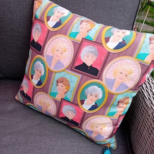 May include: A decorative cushion with a pink, blue and gold pattern featuring multiple images of women in framed portraits.