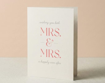 Może przedstawiać: Kremowa kartka okolicznościowa z napisem "wishing you both MRS. & MRS. a happily ever after" wydrukowanym połączeniem szarej kursywy i pogrubionej czcionki szeryfowej w kolorze koralowym, wyśrodkowanym na przedniej stronie złożonej kartki.