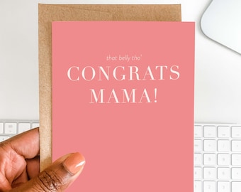 Może przedstawiać: Różowa kartka z życzeniami z białym napisem "CONGRATS MAMA!", trzymana w dłoni. Karta ma za sobą brązową kopertę, a nad głównym tekstem znajduje się napis "that belly tho'".