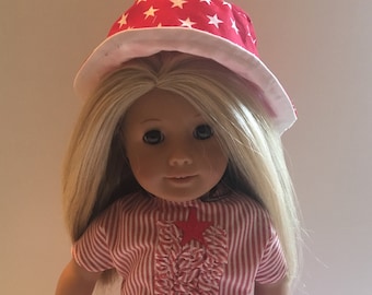 May include: A doll wearing a red and white striped outfit with a red star on the front. The doll is also wearing a red and white star patterned hat.