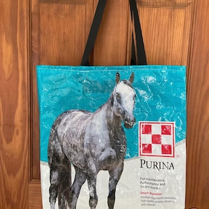 Może przedstawiać: Niebiesko-biała torba typu tote z obrazkiem konia i tekstem "PURINA" oraz "Smart Nutrition". Torba ma czarne paski i jest wykonana z materiału wielokrotnego użytku.