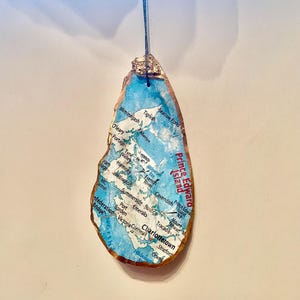 May include: A blue and white map of Prince Edward Island, Canada, printed on a seashell ornament. The map shows the location of Charlottetown, the capital city, and other towns and cities on the island.
