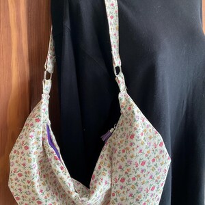 May include: A white fabric shoulder bag with a floral print. The bag has a purple zipper and a long strap.