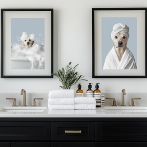 Pu&ograve; includere: Due stampe incorniciate di un cane in un bagno. Le stampe sono incorniciate di nero e mostrano un cane bianco in un bagno e un cane bianco che indossa un asciugamano bianco. Il bagno ha un doppio lavabo con due lavandini e rubinetti dorati. Ci sono asciugamani e bottiglie di sapone liquido sul bancone.