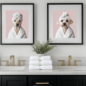 Pu&ograve; includere: Due immagini incorniciate di cani che indossano asciugamani bianchi sulla testa e accappatoi bianchi. Le immagini sono appese a una parete bianca sopra un mobile da bagno con due lavandini. Il mobile &egrave; nero con accessori dorati. Ci sono tre bottiglie di sapone per le mani sul bancone.