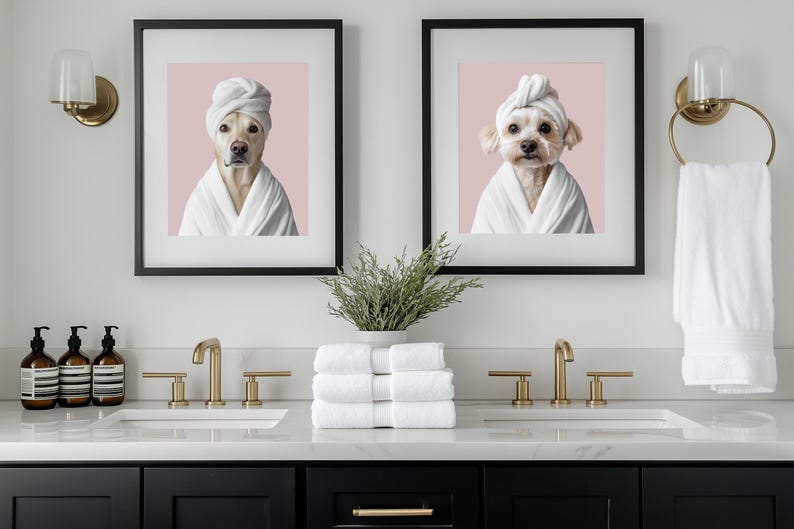 Pu&ograve; includere: Due immagini incorniciate di cani che indossano asciugamani bianchi sulla testa e accappatoi bianchi. Le immagini sono appese a una parete bianca sopra un mobile da bagno con due lavandini. Il mobile &egrave; nero con accessori dorati. Ci sono tre bottiglie di sapone per le mani sul bancone.