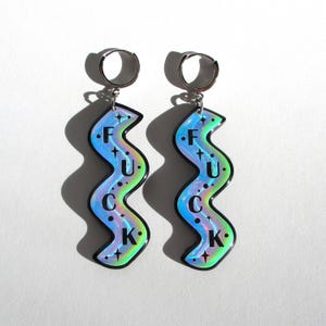 May include: A pair of silver hoop earrings with a holographic charm that says "F.U.C.K." in black letters with stars.