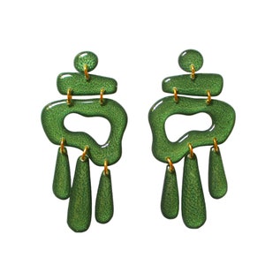 Puede incluir: Un par de pendientes verdes de diseño llamativo con un diseño abstracto único. Los pendientes presentan múltiples capas de resina verde con un acabado texturizado y detalles dorados.