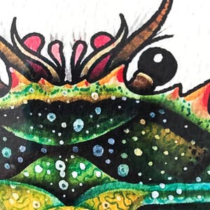 May include: Close-up of a watercolor painting of a green and yellow creature with a black eye and red and pink accents. The creature has a spiky, textured surface.