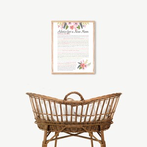 Puede incluir: Una impresión enmarcada con un diseño floral y el texto "Advice for a New Mom with All Our Love". La impresión está colgada en una pared blanca sobre una cuna de mimbre.
