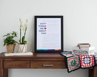 Puede incluir: Una impresión enmarcada con el texto "Sixty Things We Love About You!" sobre una mesa de madera con una caja de cerámica blanca, un letrero LOVE de metal dorado y una manta de ganchillo.