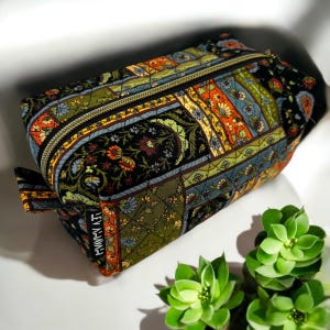 May include: A black quilted zippered pouch with a colorful floral and geometric pattern. The pouch has a gold zipper and the text "Handmade" is printed on the side.