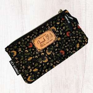 May include: Black zippered pouch with a floral pattern and a brown leather patch that says "Trust in the Lord with all your heart".