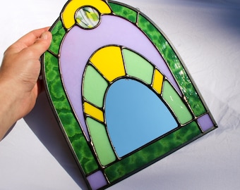 May include: A stained glass mirror with a green, purple, and yellow arched design. The mirror reflects a blue sky.