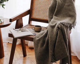 May include: A wooden chair with a woven cane seat and back, draped with a gray throw blanket. A book and a ceramic mug are on the seat.