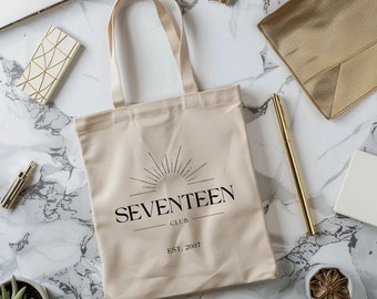 May include: A beige canvas tote bag with black text that reads "SEVENTEEN CLUB EST. 2007". The text is surrounded by a stylized sunburst design.
