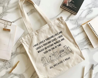 May include: A beige canvas tote bag with black text that reads "I have lived a thousand lives and loved a thousand loves. I have walked on distant worlds and seen the end of time. All because I read."  The text is accompanied by a black and white illustration of a bookshelf with books.