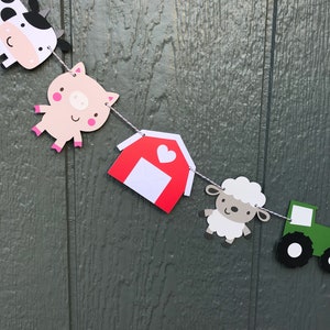 May include: A farm-themed banner with a cow, pig, red barn, sheep, and a green tractor. The banner is strung with white twine.
