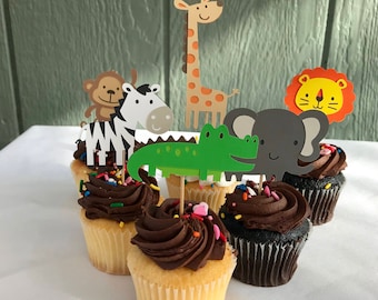 May include: Six chocolate cupcakes decorated with colorful sprinkles and topped with animal-themed cake toppers. The toppers include a zebra, a monkey, a giraffe, a crocodile, an elephant, and a lion.