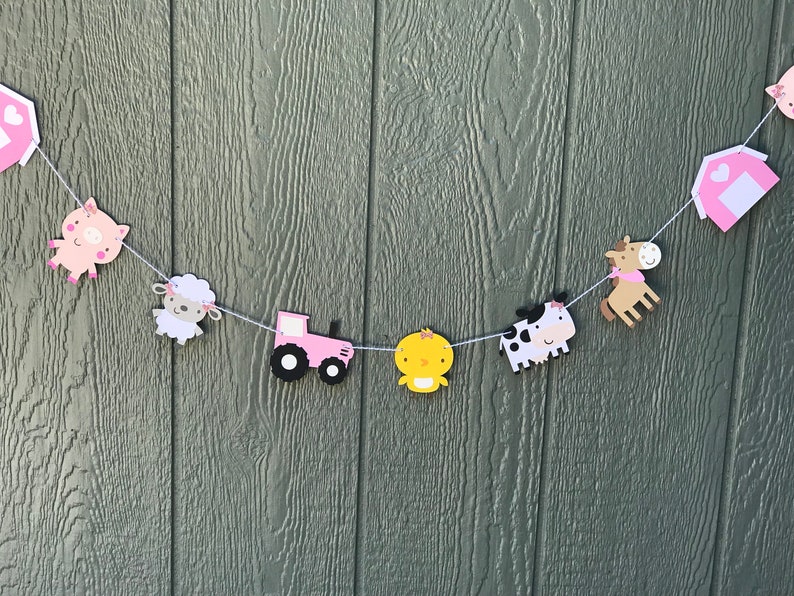 May include: A farm-themed banner with various animal and farm-related cutouts. The banner includes a pink tractor, a yellow chick, a cow, a horse, a pig, a sheep, and a barn. The cutouts are strung together with white string.