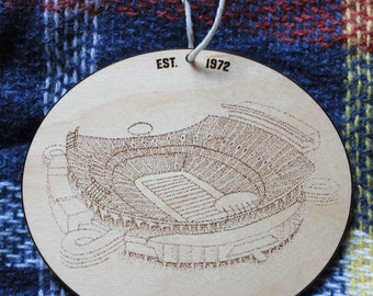 Op de afbeelding: Een ronde houten ornament met een lasergegraveerd ontwerp van Arrowhead Stadium, de thuisbasis van de Kansas City Chiefs. De ornament is lichtbruin en heeft de tekst "EST. 1972" en "ARROWHEAD STADIUM" erop.