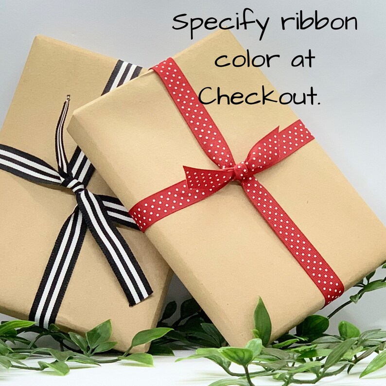 May include: Two brown gift boxes wrapped with ribbon. One box is tied with black and white striped ribbon, the other with red ribbon with white polka dots. The text "Specify ribbon color at Checkout." is written in black on a white background.