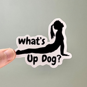 May include: A white sticker with a black silhouette of a person in an upward-facing dog yoga pose. The text "what's up dog?" is written below the silhouette.