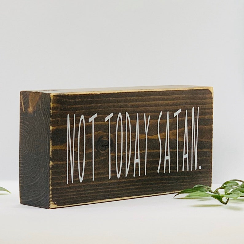 May include: A dark brown wooden block sign with the text "NOT TODAY SATAN." in white lettering.