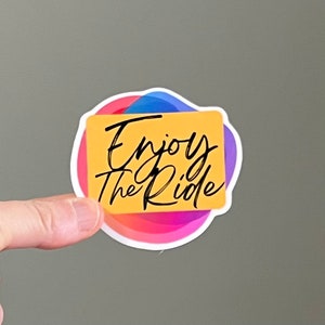 May include: A sticker with a colorful abstract design and a yellow rectangle with the text "Enjoy the Ride" in black.