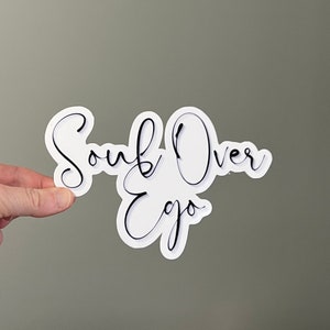 May include: White sticker with black cursive text that reads "Soul Over Ego".