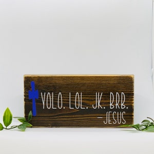 May include: A wooden sign with a blue cross and the text "YOLO. LOL. JK. BRB. -JESUS" in white lettering.