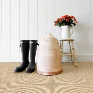 May include: Two black rain boots with a white background. A large terracotta pot with a white glaze sits on a wooden stool. A bouquet of orange roses in a white pitcher sits on the stool.