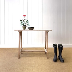 May include: A light-colored wooden table with a potted plant and a bowl on top. Black rubber boots stand on the floor in front of the table. The table is approximately 48 inches long.