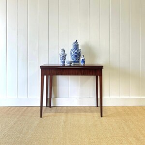 May include: A dark wood table with a drop leaf, featuring a blue and white porcelain vase and two smaller vases on top. The table is on a light brown rug.