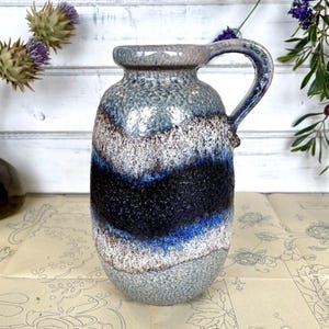 Puede incluir: Un jarrón de cerámica azul y blanco con una superficie texturizada y un cuerpo ancho y redondeado. El jarrón tiene un asa y un esmalte azul, blanco y negro.