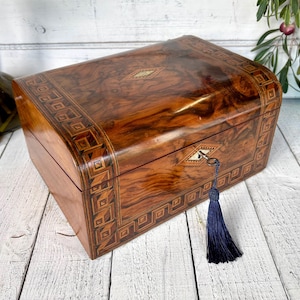 May include: A vintage wooden jewelry box with a curved top and intricate inlaid designs. The box is a rich brown color with a glossy finish, featuring a keyhole and a decorative tassel. The box is likely used for storing jewelry or other small valuables.