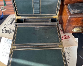 May include: An antique wooden writing desk with a green leather interior. The desk has gold accents and is open, revealing compartments and a writing surface.