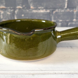 May include: A green ceramic saucepan with a single handle. The saucepan has a glossy finish and a slightly flared rim.