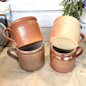 May include: Four brown stoneware mugs with handles. Two of the mugs are stacked on top of each other. The mugs are made of a rough, textured material.