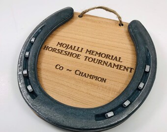 May include: A wooden horseshoe-shaped plaque with the text "Mojalli Memorial Horseshoe Tournament Co ~ Champion" engraved on it.