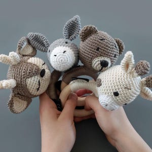 Op de afbeelding: Een houten bijtring met vier gehaakte dierenkoppen: een bruin hert, een grijs ezel, een bruine beer en een crèmekleurige giraffe.