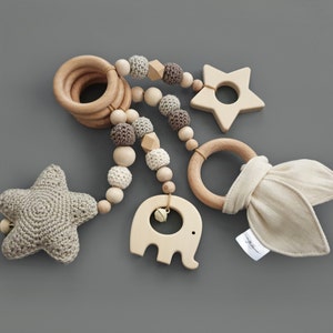 Könnte beinhalten: Ein Holzspielzeug für Babys mit verschiedenen Texturen und Formen, darunter ein Stern, ein Ring, ein Elefant und ein Stoffhase. Das Spielzeug ist mit Holzperlen und gehäkelten Kugeln aufgereiht.